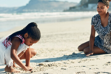 Searching for seashells. Shot of a mother and her little daughter playing in the sand at the beach.