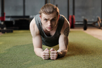 Serious male athlete standing in plank position on gym floor and looking at camera - Powered by Adobe