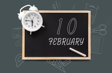 february 10. 10th day of month, calendar date.   Blackboard with piece of chalk and white alarm clock on green background. Concept of day of year, time planner, winter month