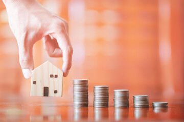 Hand picking up model house with rows stacks of coins on desk, investments, business growth, saving...