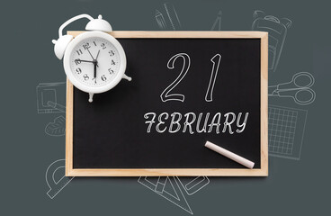 february 21. 21th day of month, calendar date.   Blackboard with piece of chalk and white alarm clock on green background. Concept of day of year, time planner, winter month