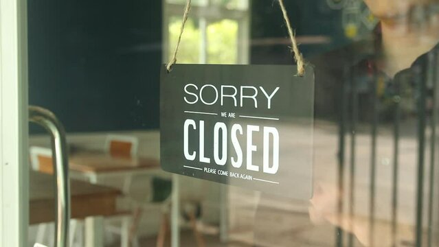 Man changes an open sign to a closed sign on glass door