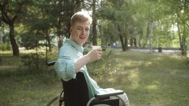 A young disabled man in a blue shirt is drinking his beverage and looking at the camera and smiling 