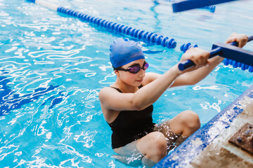 hispanic teenager girl swimmer athlete wearing cap and goggles in a swimming training at the Pool...