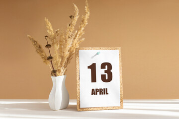 April 13. 13th day of month, calendar date.White vase with dried flowers on desktop in rays of...