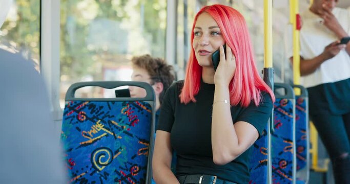 Young woman with pink hair rides bus , girl talking on smartphone, running business errands, doctor's appointment, gossiping with friend, phone conversation in public place