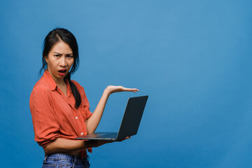 Young Asia lady using laptop with negative expression, excited screaming, cry emotional angry in casual cloth and stand isolated on blue background with blank copy space. Facial expression concept.