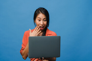 Young Asia lady using laptop with positive expression, smiles broadly, dressed in casual clothing feeling happiness and stand isolated on blue background. Happy adorable glad woman rejoices success.