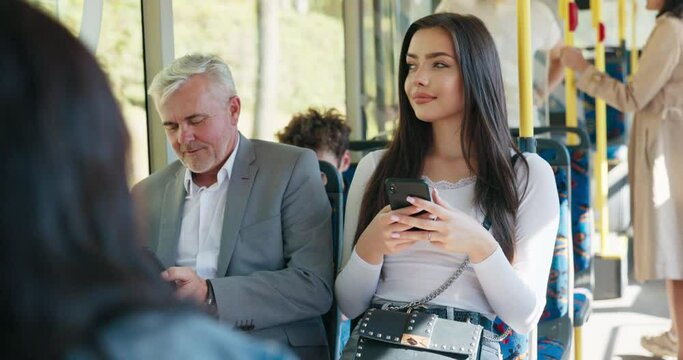 Beautiful brunette girl is holding phone and browsing social media student on way back from university by bus older man