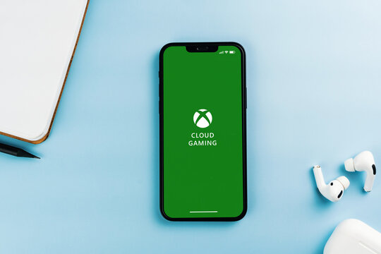 Xbox Cloud Gaming app on the smartphone screen. Blue background with notepad and AirPods. Rio de Janeiro, RJ, Brazil. April 2022