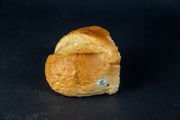 A piece of moldy bread against a black background. A stale piece of wheat loaf.