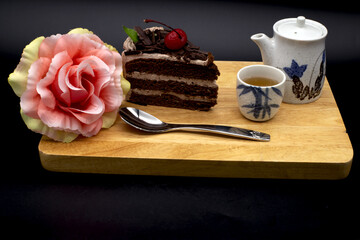 Chocolate cake with cherries and tea on a wooden tray in black background. Include Clipping Path.