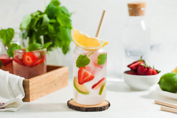A refreshing summer drink with strawberries, lemon and mint in a glass on a light background. Strawberry lemonade