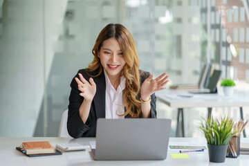 Obraz premium Beautiful young Asian businesswoman sitting looking at webcam, looking at camera, during virtual meeting or video call talk.