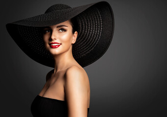 Cheerful Smiling Woman in Summer Hat. Beauty Model in Big Black Hat and Dress. Fashion Girl Face Portrait with Red Lipstick. Elegant Lady over dark Gray Background