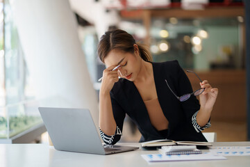 Obraz premium Overworked and stressed young Asian woman sitting at workplace in office.
