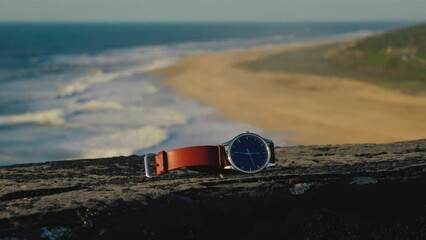 Seamless video loop Cinemagraph of a wrist watch clock lying on a reeling by a seasoned ocean beach close to Lisbon, Portugal  with a blurry background on a sunny afternoon. Time is standing still. - Powered by Adobe