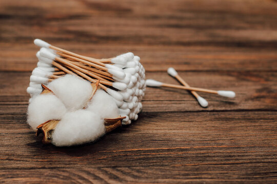 Cosmetic eco sticks on a cardboard base are scattered with cotton on a wooden background.