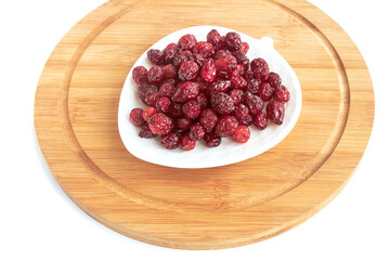 A delicious dried wholesome wild berry cranberry lies on a white plate, a kitchen wooden board on a white background.