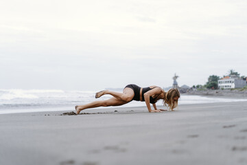 Sporty woman doing mountain climber exercise - run in plank to burn fat. Sunset beach, blue sky...