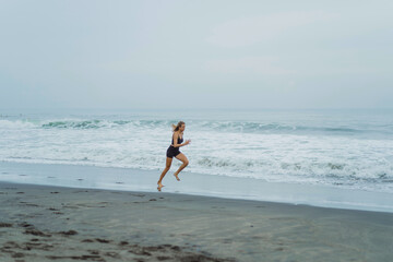 Fototapeta premium A barefoot young woman with a slender body runs on the sea surf by the water pool to keep fit and burn fat. Women's fitness, jogging, sports activities on a summer.