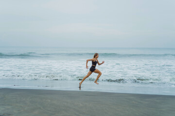 A barefoot young woman with a slender body runs on the sea surf by the water pool to keep fit and burn fat. Women's fitness, jogging, sports activities on a summer.