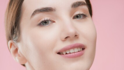 Obraz premium Extreme close-up beauty portrait of young fit attractive Caucasian woman with brown who smiles and looks at camera against pink background | Skin care concept