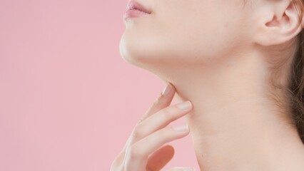 Big close-up shot of young Caucasian woman who touches her neck with her fingers on pink background | Beauty care commercial concept
