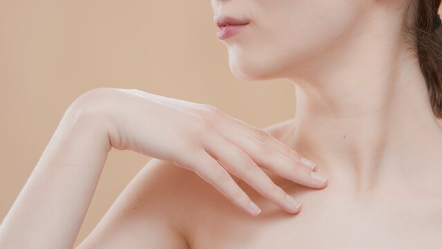 Close-up beauty portrait of Caucasian woman touches her clavicle turning her head aside on beige background | Beauty care commercial concept