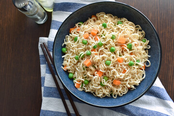 Instant noodles with carrots and peas in a blue bowl. Vegetarian food style concept.  Healthy and dietary food from above.  Flat lay top view photo. 