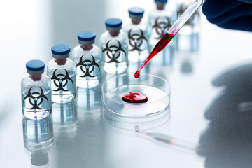 Secret genetic testing of warfare in a labs. A pipette and a Petri dishes with human blood sample and a row of ampoules with a bio-hazard sign, close-up, selected focus.
