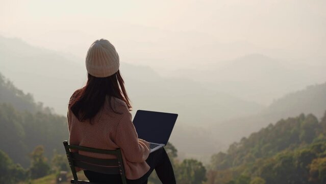 Young woman freelancer traveler working online using laptop and enjoying the beautiful nature landscape with mountain view at sunrise