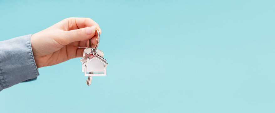Banner of mortgage with copy space. Female hand holding key and house keychain. Turquoise background. Concept of insurance and leasing of real estate