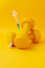 syringe stuck in a dumbbell, a medical ampoule lies next to it, a yellow background, a vertical...