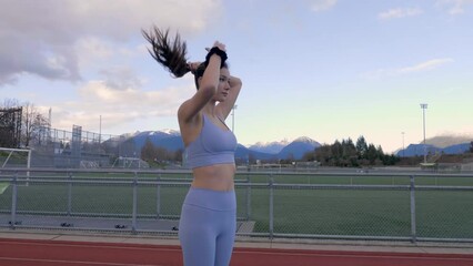 Athletic young woman pulling hair back into bun on track and field