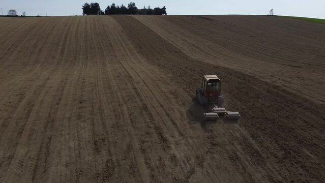 Drone follow a red small tractor in rolling soil operation for seedbed preparation in uphill countryside agricultural farm 
