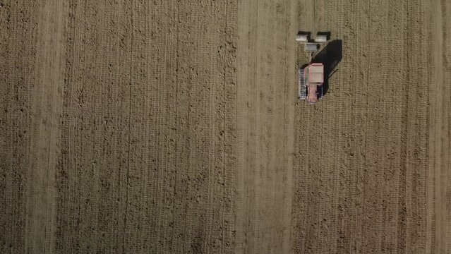 Aerial top down of red tractor pull a three rolling soil system plowing and preparing the land before seeding process, drone agricultural footage food chain market crisis concept