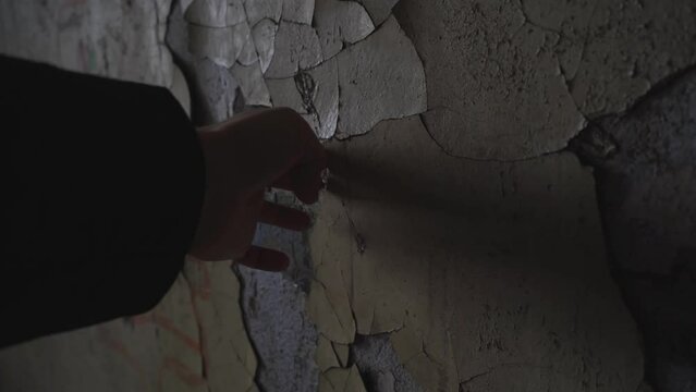 a man's hand picks off the old paint. streak peeling paint on a wall in a ruined abandoned building