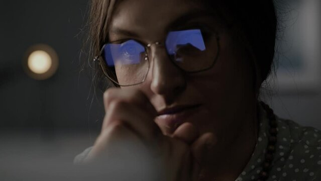 Woman thinks and looks at computer, screen is reflected in glasses. Close-up of pensive freelancer looking for inspiration and new ideas. Remote worker makes difficult decision