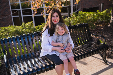 Portrait of smiling middle aged mother sitting on metal bench with young son in her lap
