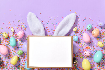 A mockup with an envelope, rabbit ears and Easter eggs on a purple background with colored splashes.