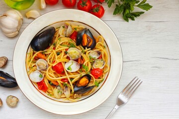 Italian Traditional Dish"Spaghetti alle cozze e vongole",spaghetti with mussels,clams,cherry tomatoes,garlics,olive oil,white wine,parsley and peppers on plate with white wood background.Top view