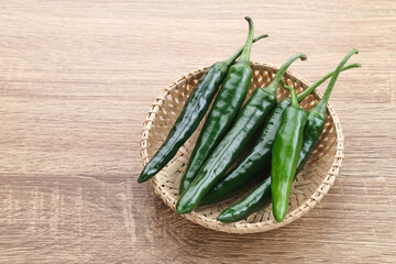 Green chili served in bamboo plate on wooden table.
