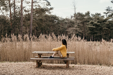young woman sitting on picnic bench by a pond and trees