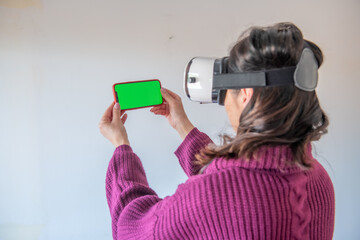 Virtual reality concept. Woman wearing VR helmet and holding smartphone with green screen, isolated on white background