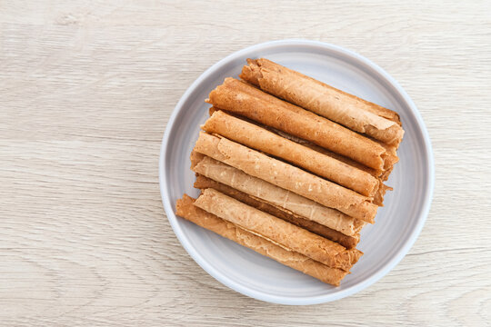 Waffle egg rolls or semprong cake, a traditional Indonesian snack with a unique shape like a layered pipe, served on a white plate. Selected focus.
