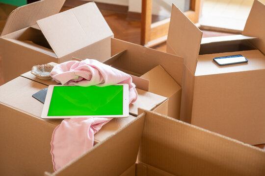 Empty cardboard boxes ready to be open along with a tablet with green screen, moving to a new home concept.