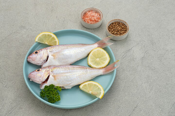 Yellow Croaker Fish, Ikan Ekor Kuning, served on blue plate with spices and lemon. Selected focus
