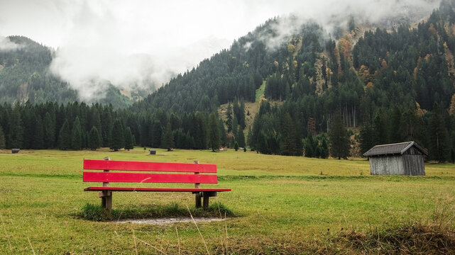 red bench in alpine countryside. Foggy mountains in Tyrol. 