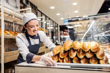 A happy saleswoman putting pastry ready for sale at supermarket.